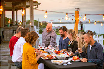 Group of people eating seafood on a deck at sunset
