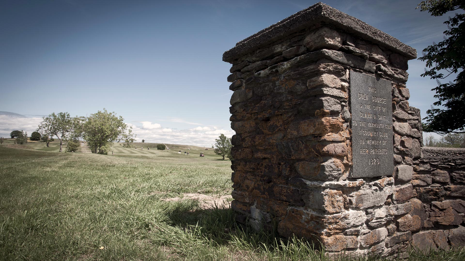 A stone fence with a plaque in front of a golf green